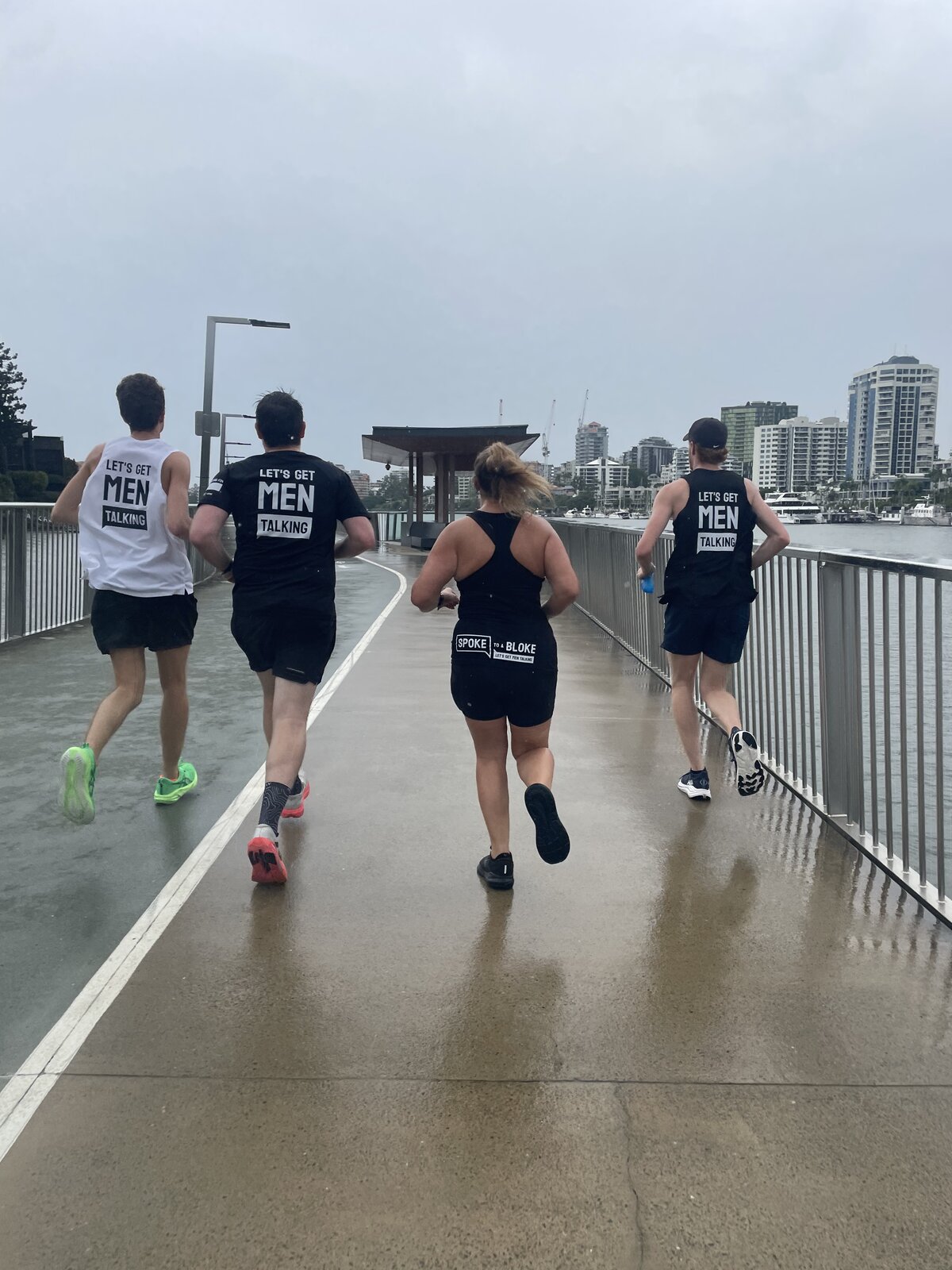 Runners in Let's Get Men Talking singlets on a riverside path in the rain